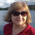woman with sunglasses and short hair smiling in front of a lake