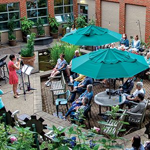 A concert in a courtyard. People gathered in chairs under tents watching a person in front perform.
