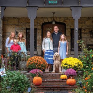 family and dog on front porch of home with flowers and pumpkins