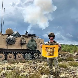 military man with terrible towel in front of tank