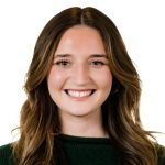 A smiling woman with long, wavy brown hair is wearing a dark green sweater against a plain white background.
