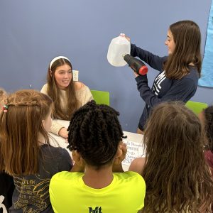 teen girl holding a plastic milk jug in front of other kids
