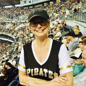 woman with glasses and baseball hat smiles at game