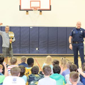 firefighter and gym teacher talk to kids in a school gym