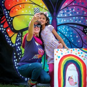 woman and girl take selfie in front of rainbow butterfly mural at pride celebration