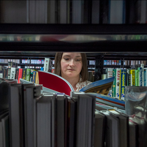 woman reading book through library shelves