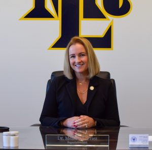 woman sitting at desk smiling with MTL school logo on the wall behind her