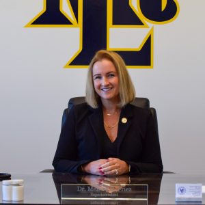woman sitting at desk smiling with MTL school logo on the wall behind her