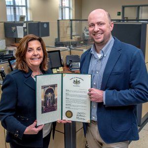 man and woman smile holding a certificate in an office