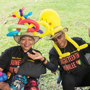 two people with balloon animal hats smiling and wearing Juneteenth Jubilee shirts