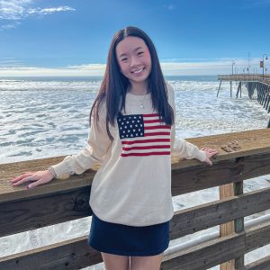 girl wearing American flag sweater smiles in front of ocean