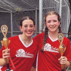 two girls in red softball uniform holding trophies