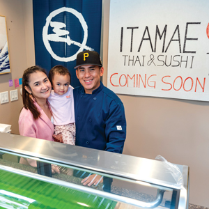 A man and a woman holding a young child standing in their storefront