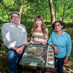 a man, a young woman and an older woman standing in a park in front of a sign