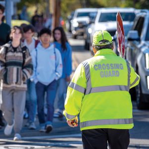 A crossing guard wearing a bright yellow jacket allowing kids to cross the crosswalk