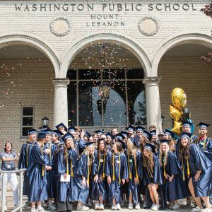 high school students in cap and gown outside of school with confetti