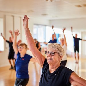 Smiling senior woman in sportswear doing an aerobics exercise class with other seniors in a health club