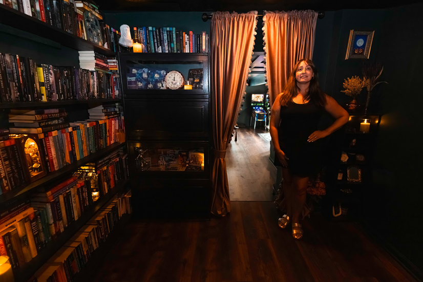 A woman standing in a dark room with shelves surrounded by books, and sculptures, and nick-nacks on the shelves