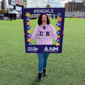 woman smiling in purple hoodie holding end ALZ sign on a field