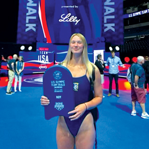 A woman standing in front of a US Olympic sign holding an award