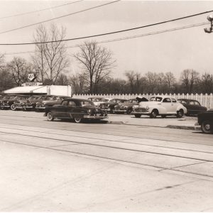 A black and white photo of a used car lot in 1919. Classic cars line the side of the road.