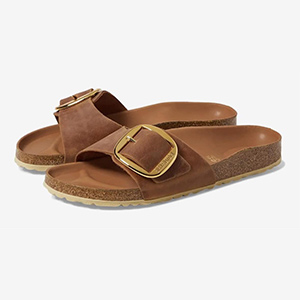 A pair of brown sandals with gold buckles on the straps on a white background.