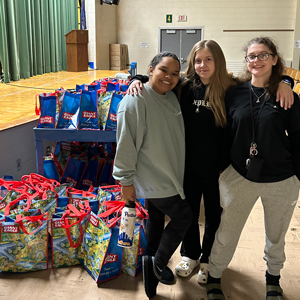 three teenage girls standing next to bagged food for a food drive