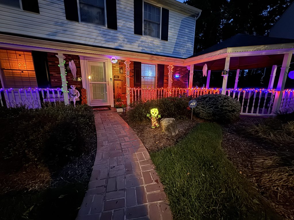 green happy skeleton Halloween decoration lit up at night in front yard of house with other decorations