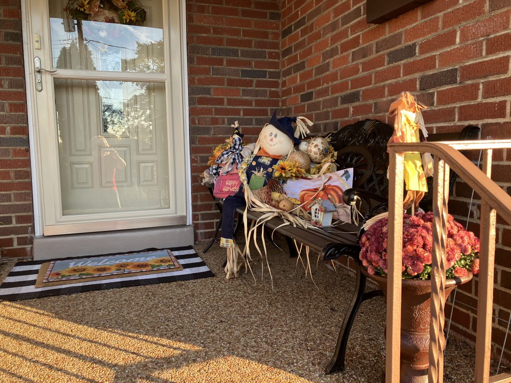 porch of home with scarecrows and fall decorations and red mums