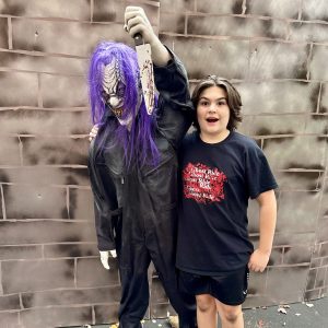 boy looking surprised with a Halloween life-size decoration holding a bloody knife and purple hair