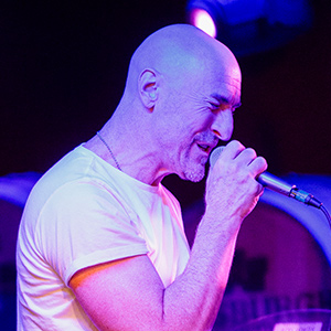 Profile shot of a man holding a microphone and singing passionately wearing a white t-shirt.