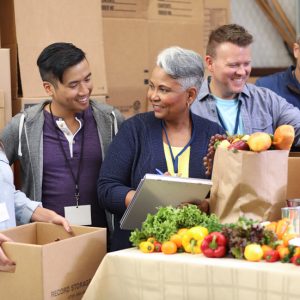 a diverse group of people smiling and gathering fresh food into boxes and bags