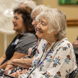 Side shot of a group of casually dressed older women sitting in chairs smiling.
