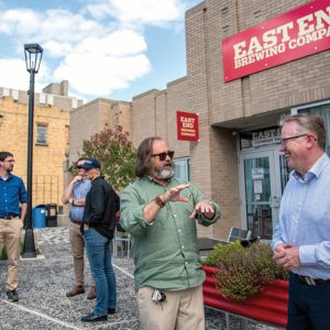 Several men dressed in business casual attire, standing outside of the east end brewing company talking to each other.