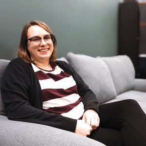 A woman wearing glasses and a stripped shirt sitting on a couch smiling