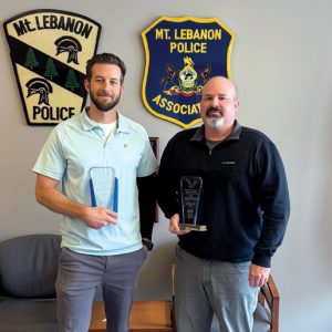 Two men standing next to an American flg in a police station holding awards