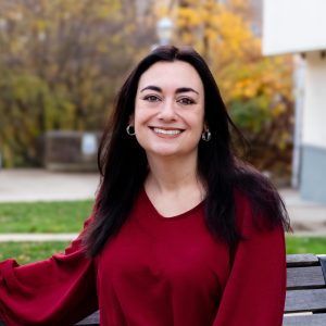 woman with red shirt smiling on bench with fall folliage