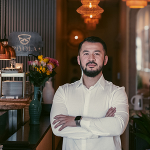 man with arms crossed in restaurant. Piyola sign in background