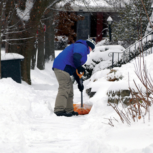 man shoveling snow on sidewalk in winter gear