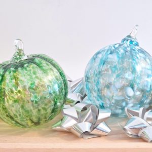 a green and a blue glass blown ornaments sitting next to some bows