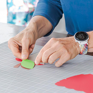A close up of a hands putting assembling a paper apple.