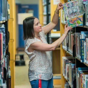A woman picking a book from a library shelf