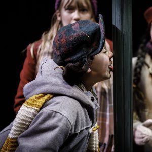 image from a play with five children in winter clothes. one has his tongue stuck to a pole