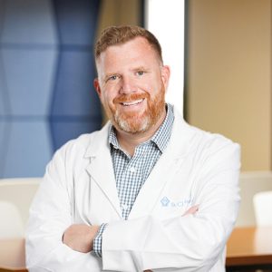 doctor with beard and white jacket smiling with arms crossed