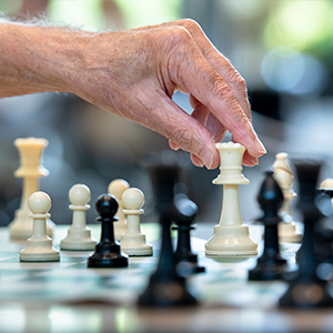 A close up of a hand holding a white chess piece surrounded by white and black chess pieces. The pieces in the front and back are in soft focus.