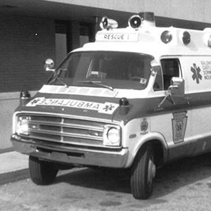 Black and white photo of an ambulance parked in front of a building.