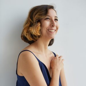 Smiling headshot of a woman looking into the distance. Short hair and blue top.