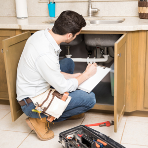 Man with clipboard and tool box looking under kitchen sink