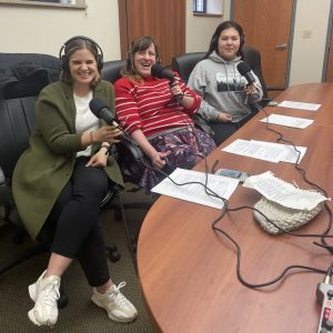 Two women and a teenager wearing headphones and holding microphones.