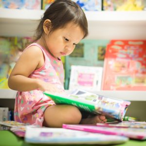 A small child reading next to a stack of books.
